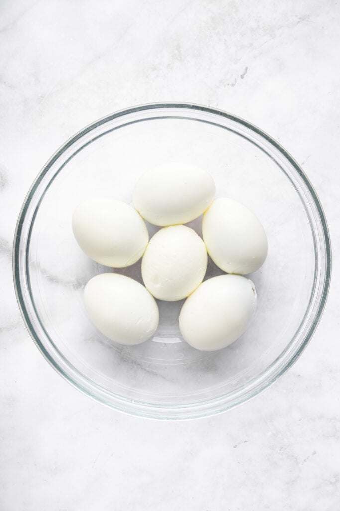 6 peeled hard-boiled eggs in glass bowl.