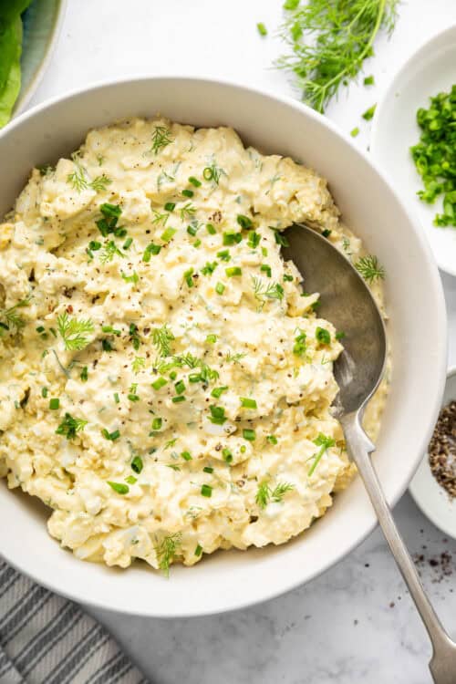 Egg salad in bowl with fresh herbs for garnish.