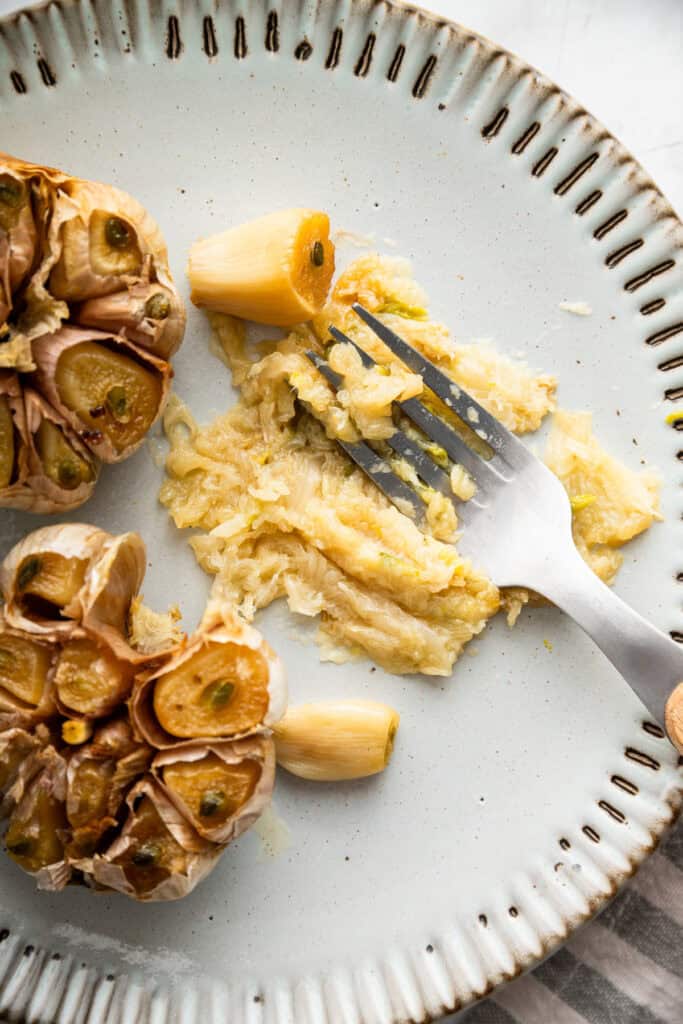 Fork mashing oven roasted garlic on plate.