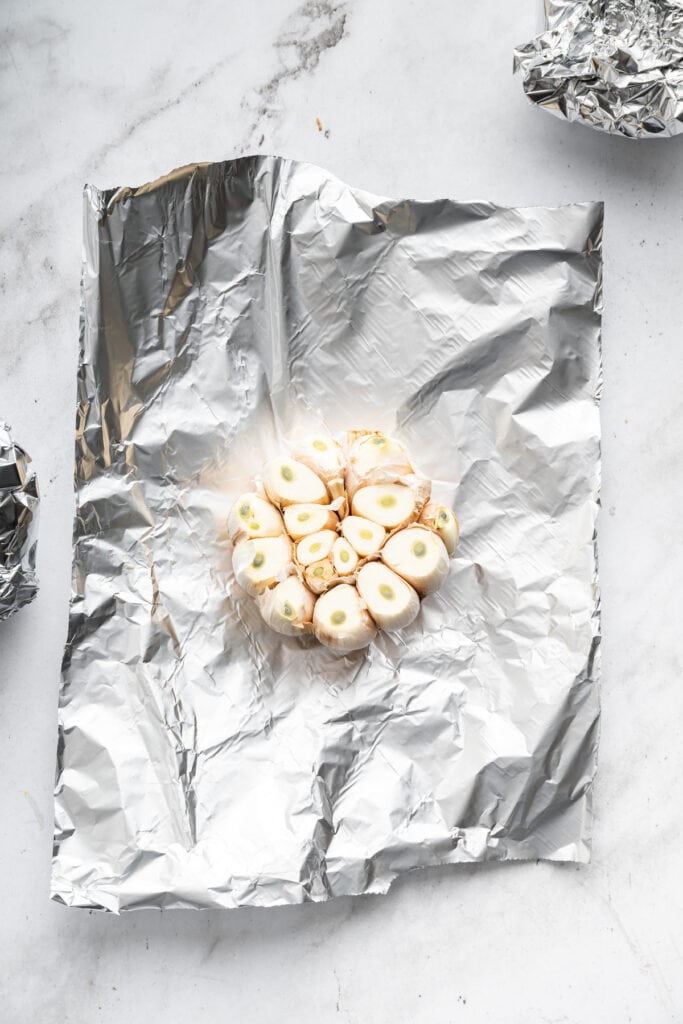 Head of garlic with top cut off, sitting on sheet of foil.