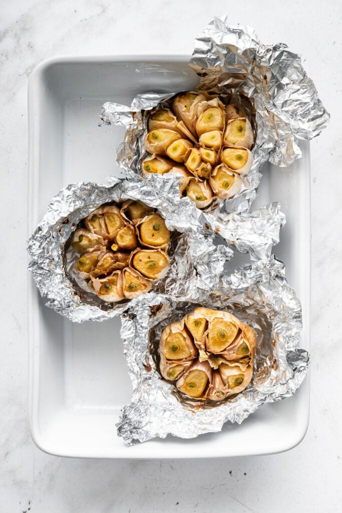 Oven roasted garlic in foil set in baking dish.
