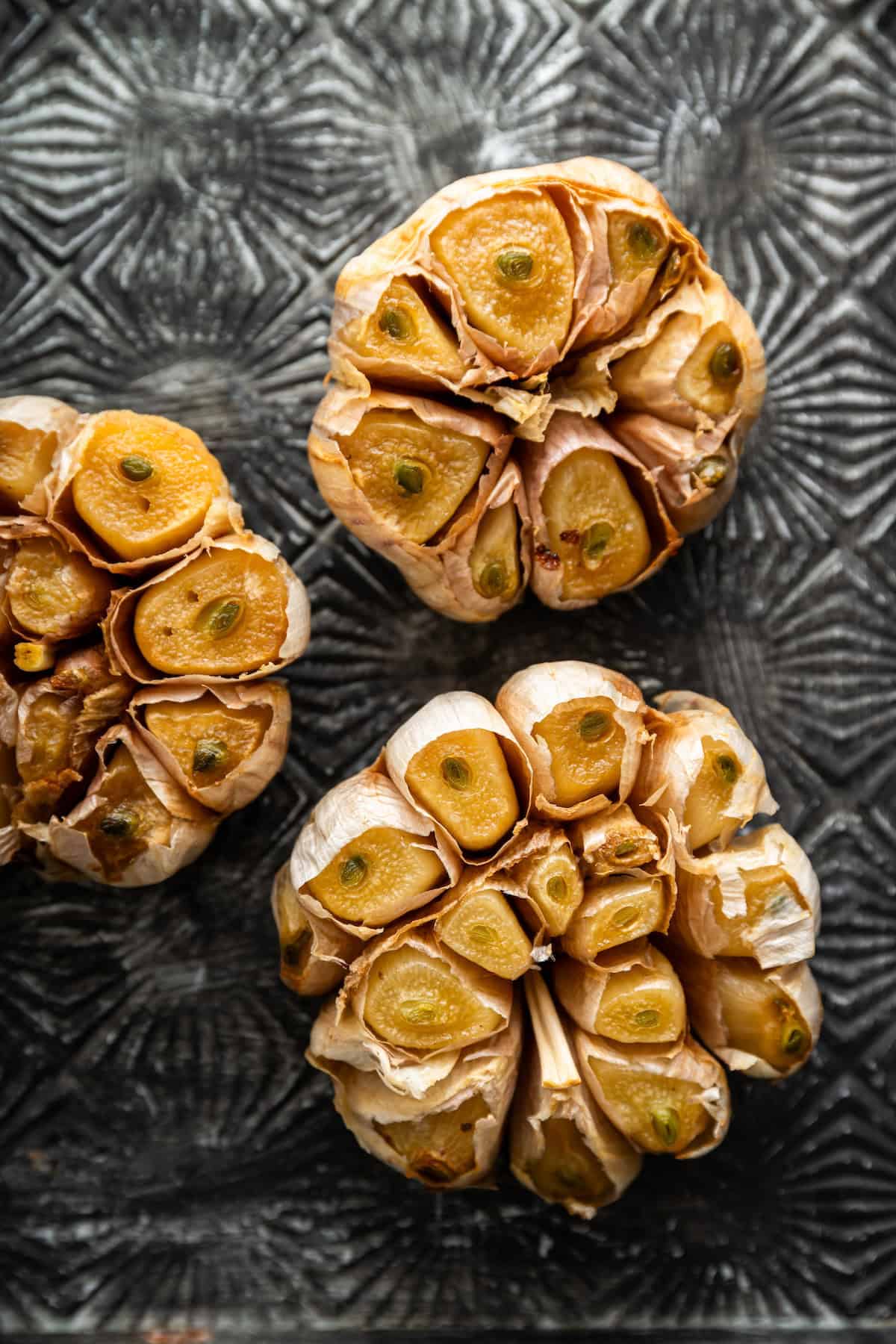 Three heads of roasted garlic on sheet pan.