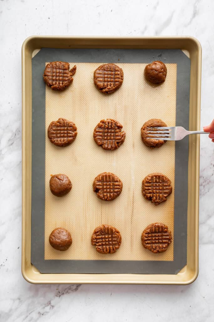 These easy almond butter cookies are made with just 5 ingredients! Naturally gluten-free, chewy with crisp edges, and full of nutty flavor. Pressing fork into almond butter cookie dough to create crosshatch pattern