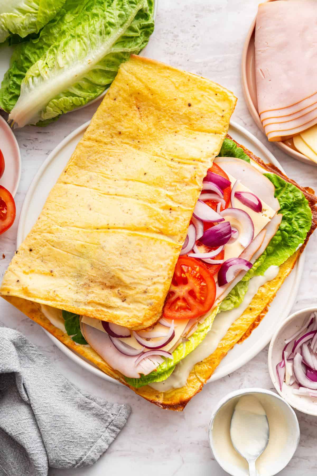 These high protein cottage cheese wraps are made with eggs and pantry seasonings—that’s it. An easy low carb alternative that tastes delish! Folding over cottage cheese wrap with veggies and lunchmeat on plate.