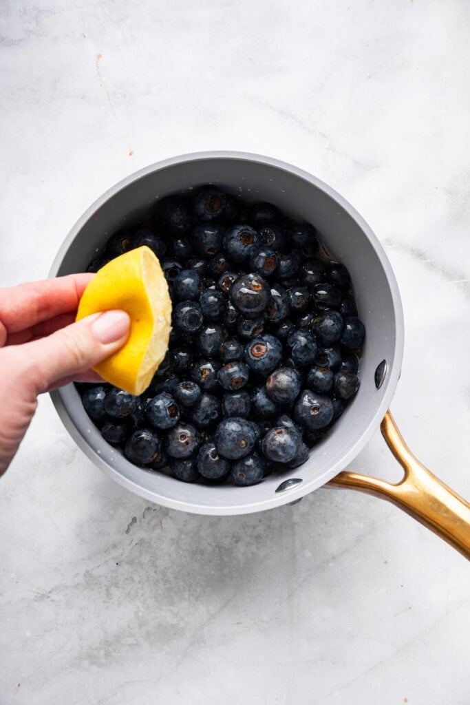 Sweet, jammy berries simmer into a quick blueberry compote that instantly upgrades pancakes, yogurt, desserts, and more. Just 3 ingredients! Squeezing lemon juice into pan of blueberries.