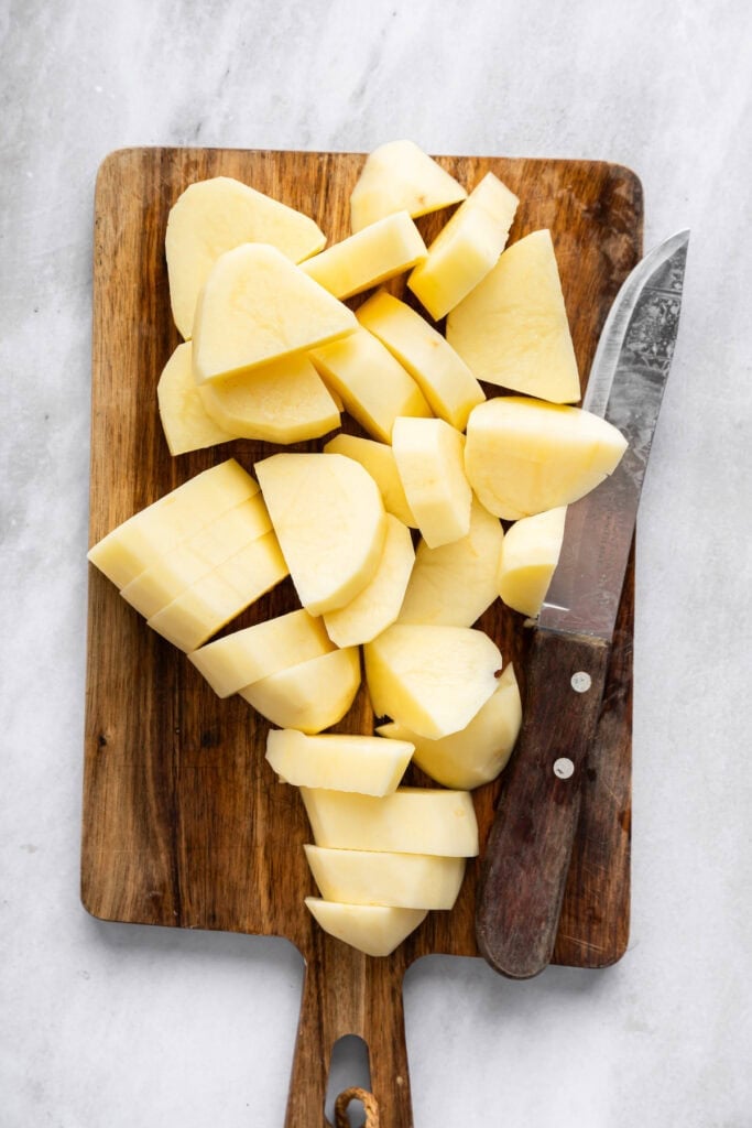 Cut potatoes on wooden board with knife.