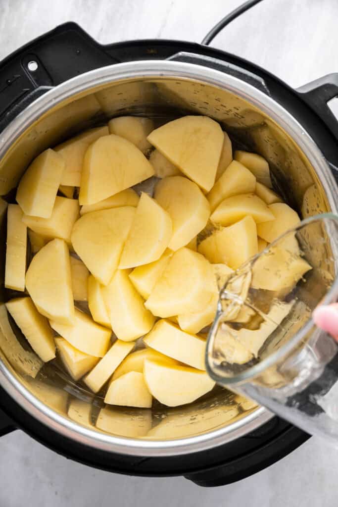 Pouring water into Instant Pot with potatoes.