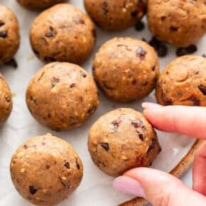 Hand picking up peanut butter protein ball from plate.