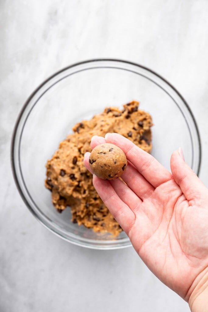 Hand holding peanut butter protein ball over bowl of dough.