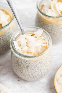 Small jars of coconut chia pudding topped with cashew butter and coconut flakes.