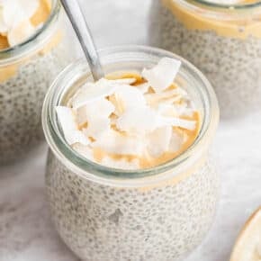 Small jars of coconut chia pudding topped with cashew butter and coconut flakes.