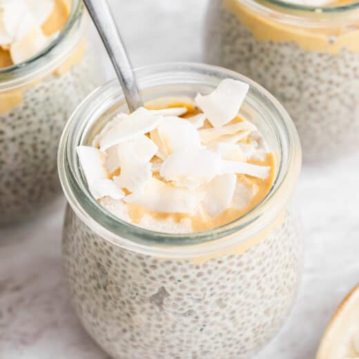 Small jars of coconut chia pudding topped with cashew butter and coconut flakes.