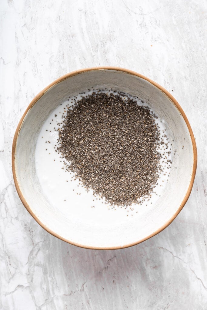 Adding chia seeds to a bowl with coconut milk.
