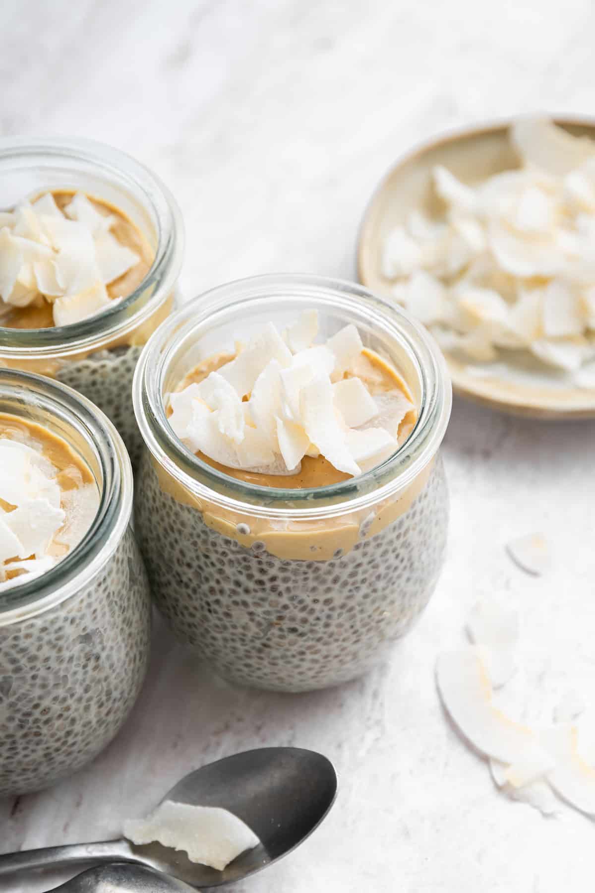 Several jars of chia pudding made with coconut milk and topped with cashew butter and coconut flakes, ready to be enjoyed