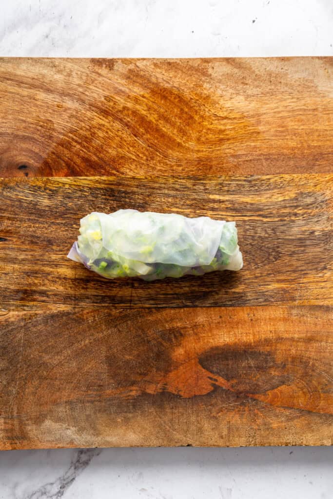 On warm days, this summer rolls recipe is a must. Crisp veggies and avocado are wrapped in rice paper for a refreshing, no-cook meal. A summer roll on a cutting board.