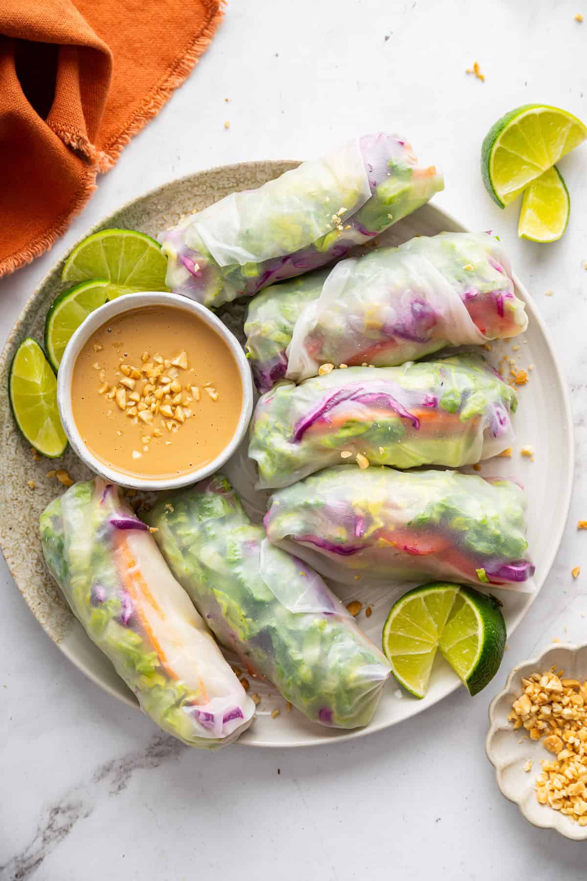 On warm days, this summer rolls recipe is a must. Crisp veggies and avocado are wrapped in rice paper for a refreshing, no-cook meal. Summer rolls arranged on a plate with peanut dipping sauce.