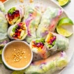 Summer rolls arranged on a plate with peanut dipping sauce. 2 are cut in half to reveal the inside.