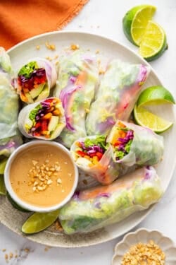 Summer rolls arranged on a plate with peanut dipping sauce. 2 are cut in half to reveal the inside.