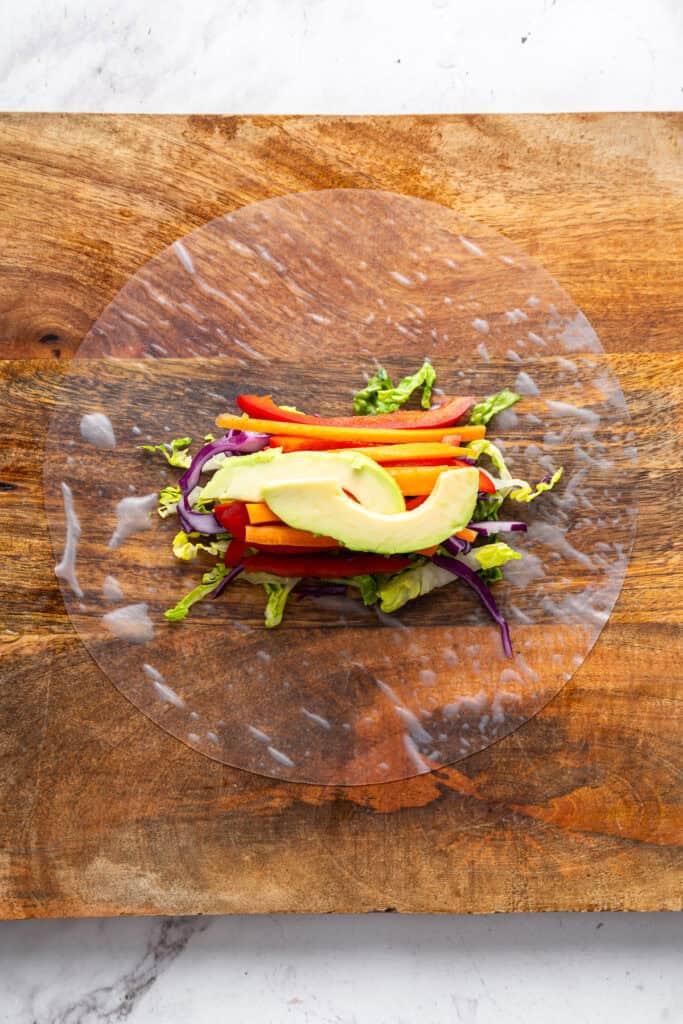 On warm days, this summer rolls recipe is a must. Crisp veggies and avocado are wrapped in rice paper for a refreshing, no-cook meal. A hydrated rice paper wrapper with veggies and avocado on top.