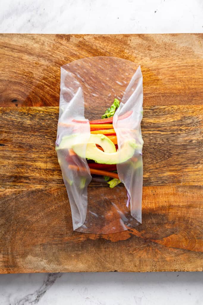 On warm days, this summer rolls recipe is a must. Crisp veggies and avocado are wrapped in rice paper for a refreshing, no-cook meal. Folding opposing sides of a rice paper wrap around veggies and avocado.
