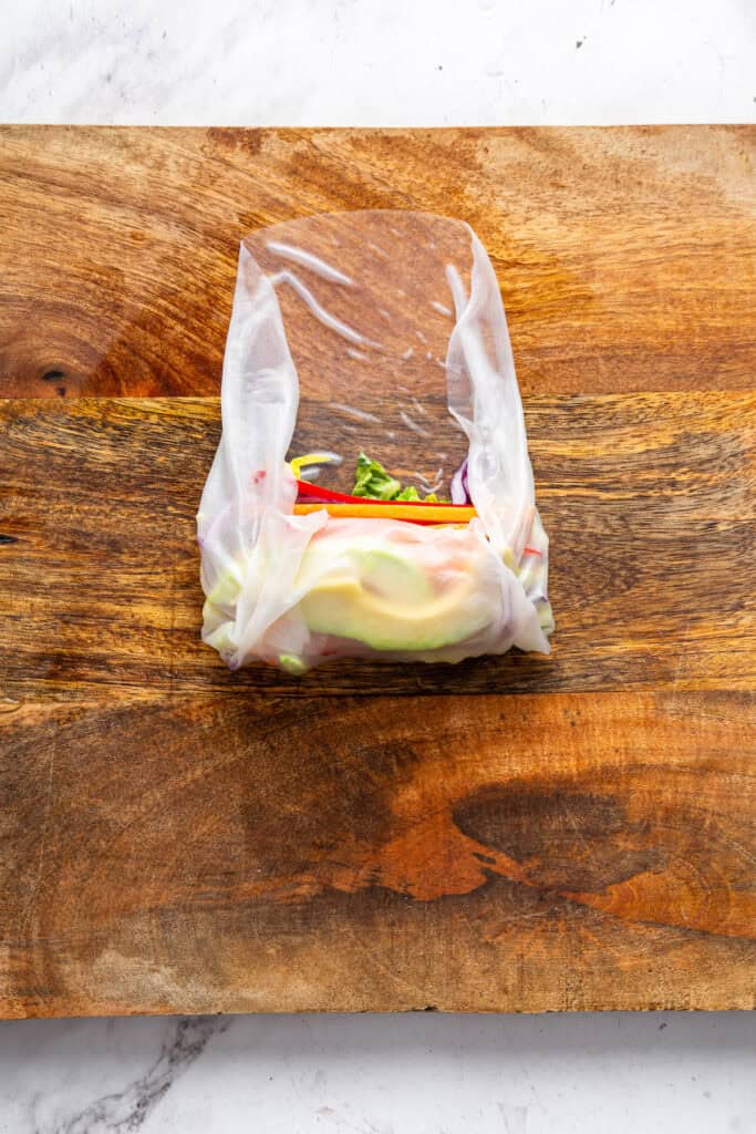 On warm days, this summer rolls recipe is a must. Crisp veggies and avocado are wrapped in rice paper for a refreshing, no-cook meal. Wrapping a rice paper wrap around veggies and avocado to make a summer roll.