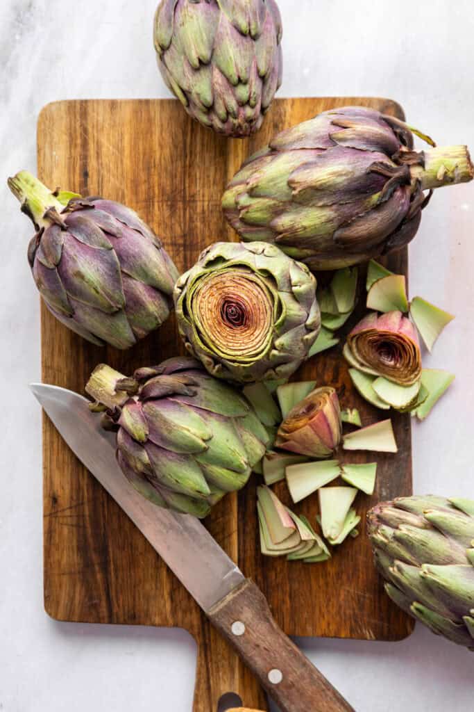 Cutting the tips off the leaves of raw artichokes.