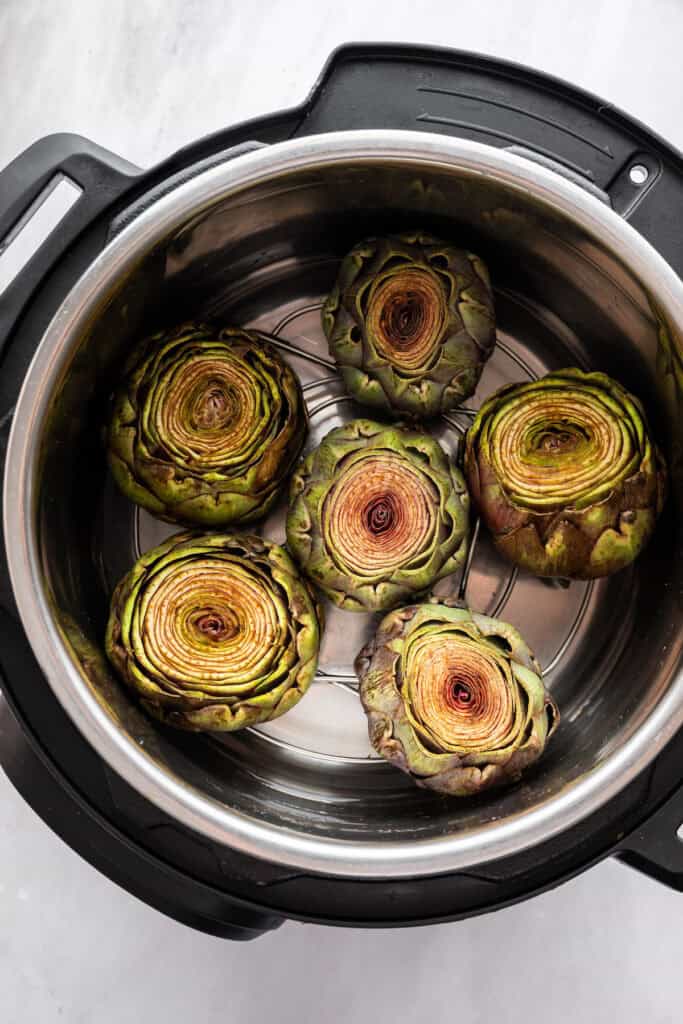 Artichokes in a steamer basket in an Instant Pot with some water.