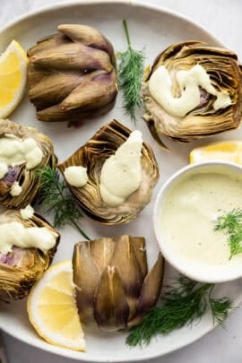 Halved steamed artichokes with lemon dill sauce.