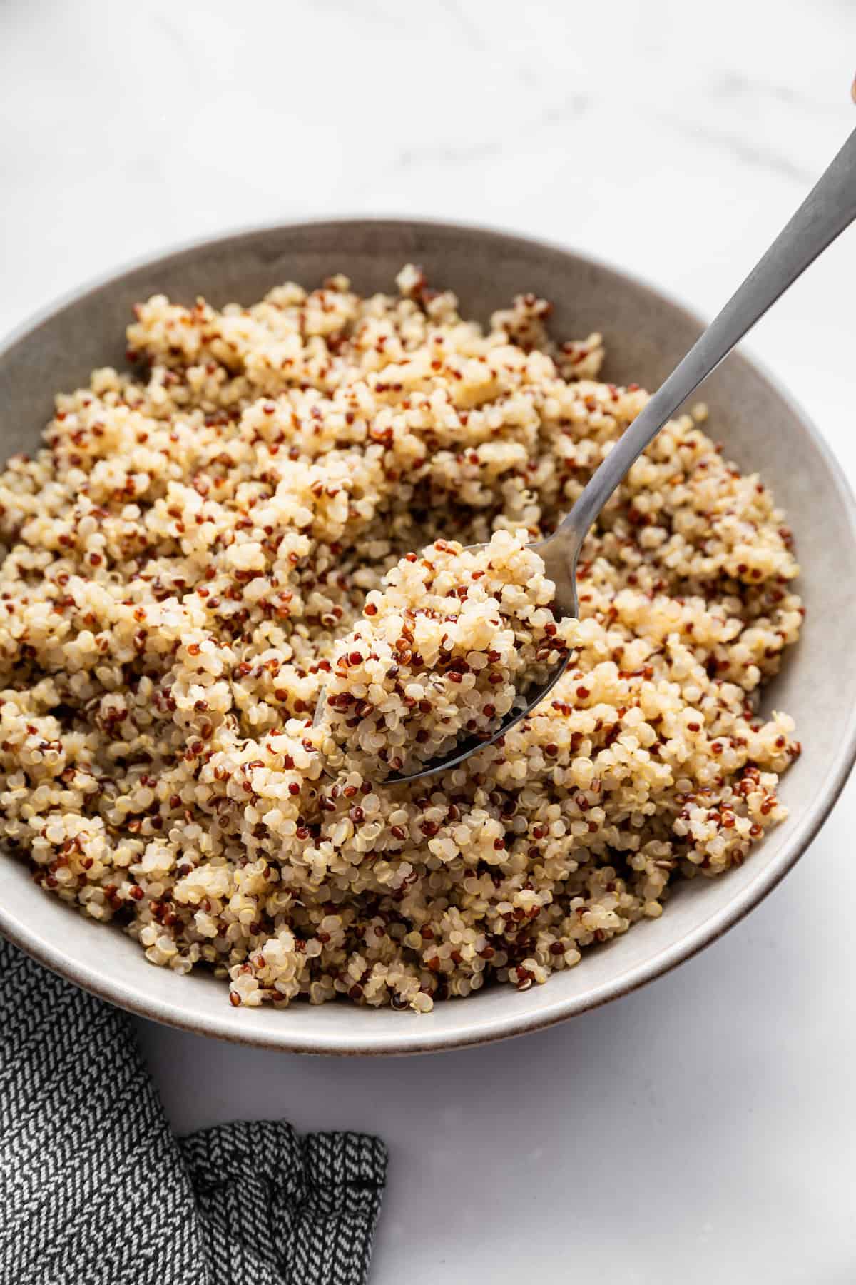 A spoon listing fluffy Instant Pot quinoa from a bowl.