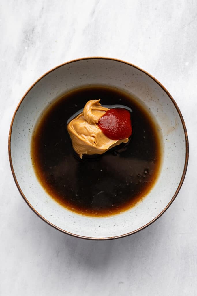 This 4-ingredient peanut sauce recipe yields a smooth, savory, tangy sauce with the perfect spice kick. Ditch the takeout. Make it at home! Soy sauce, peanut butter, sriracha, and lime juice in a bowl.
