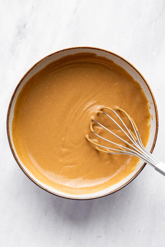 This 4-ingredient peanut sauce recipe yields a smooth, savory, tangy sauce with the perfect spice kick. Ditch the takeout. Make it at home! Peanut sauce in a bowl with a whisk.
