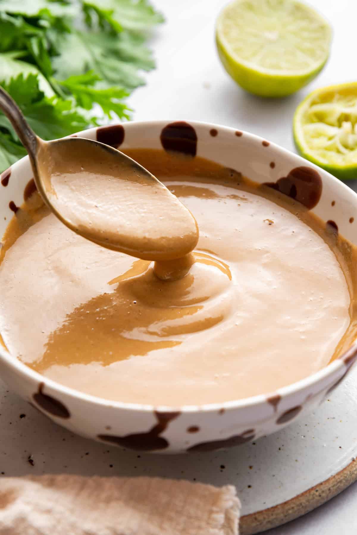 This 4-ingredient peanut sauce recipe yields a smooth, savory, tangy sauce with the perfect spice kick. Ditch the takeout. Make it at home! A spoon dipping into a bowl of peanut sauce.