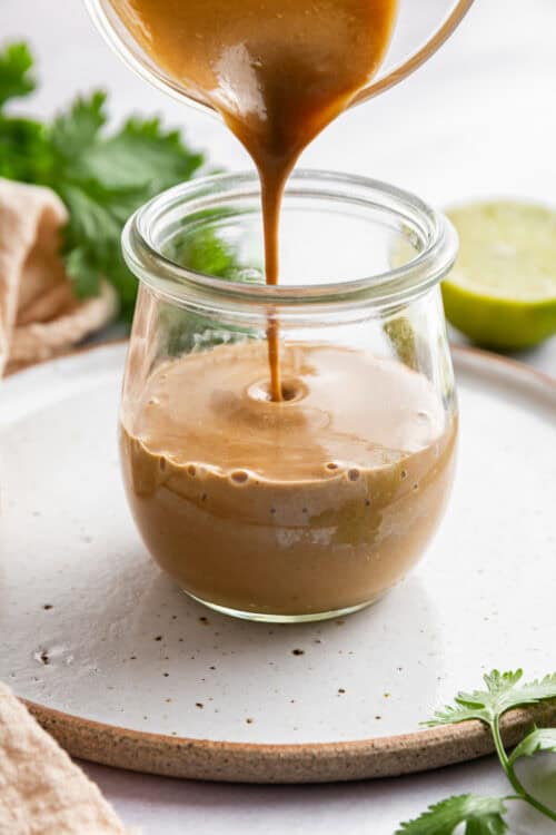 Drizzling peanut sauce into a jar.