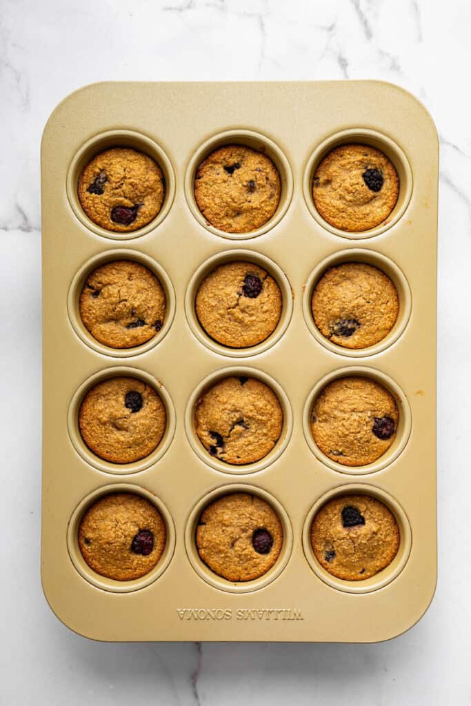 Topped with a smooth coconut-lime glaze, these easy, tender, GF blackberry muffins are a fabulous way to celebrate berry season. Blackberry muffins cooling in a muffin pan.