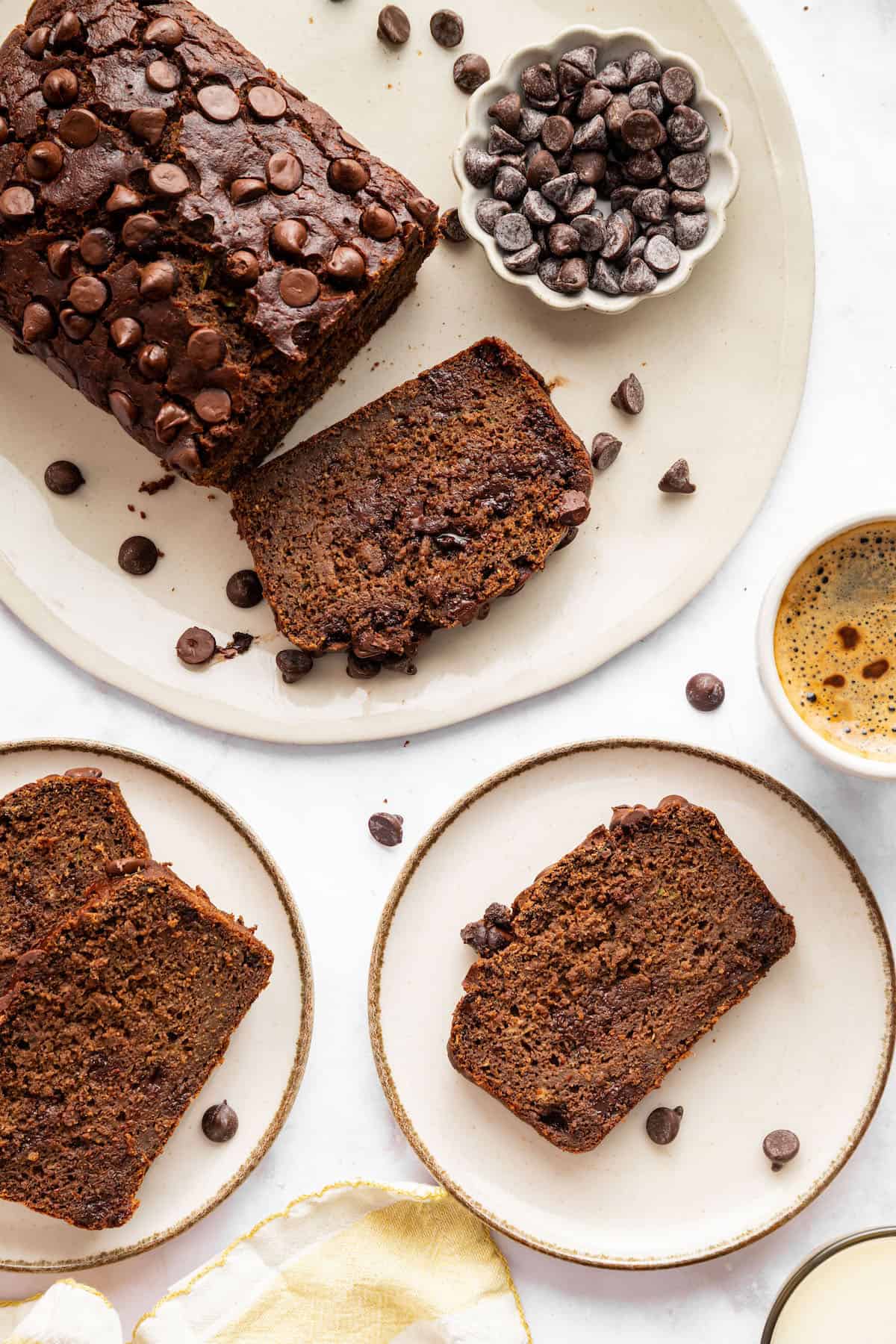 This vegan chocolate chip zucchini bread is incredibly tender, and the rich, earthy chocolate-zucchini combo is to die for. A loaf of chocolate zucchini bread and a couple of plates loaded up with slices.