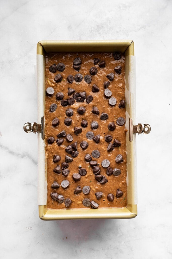 This vegan chocolate chip zucchini bread is incredibly tender, and the rich, earthy chocolate-zucchini combo is to die for. A loaf pan full of vegan, gluten-free chocolate zucchini batter topped with chocolate chips.