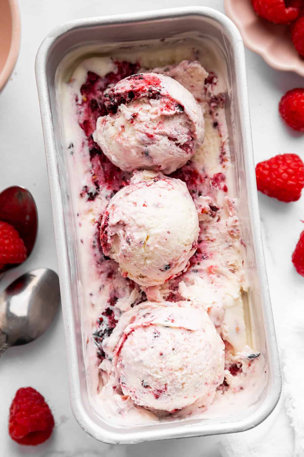 This Greek yogurt ice cream is smooth, creamy, packed with protein, and lightly sweetened with honey and a colorful swirl of fresh berries. A tub of Greek yogurt ice cream with three scoops sitting on top.