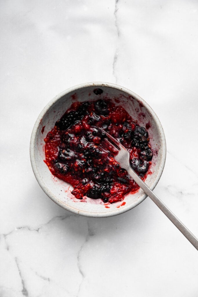 This Greek yogurt ice cream is smooth, creamy, packed with protein, and lightly sweetened with honey and a colorful swirl of fresh berries. Mashing berries with a fork.