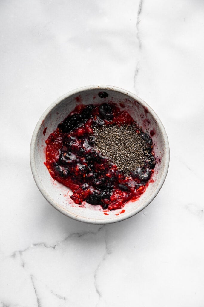 This Greek yogurt ice cream is smooth, creamy, packed with protein, and lightly sweetened with honey and a colorful swirl of fresh berries. Adding chia seeds to a bowl of mashed berries.