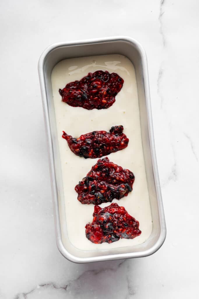 This Greek yogurt ice cream is smooth, creamy, packed with protein, and lightly sweetened with honey and a colorful swirl of fresh berries. Adding dollops of berry-chia seed swirl to a base of Greek yogurt ice cream in a loaf pan.