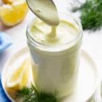 A spoon dipping into a jar of dill sauce.