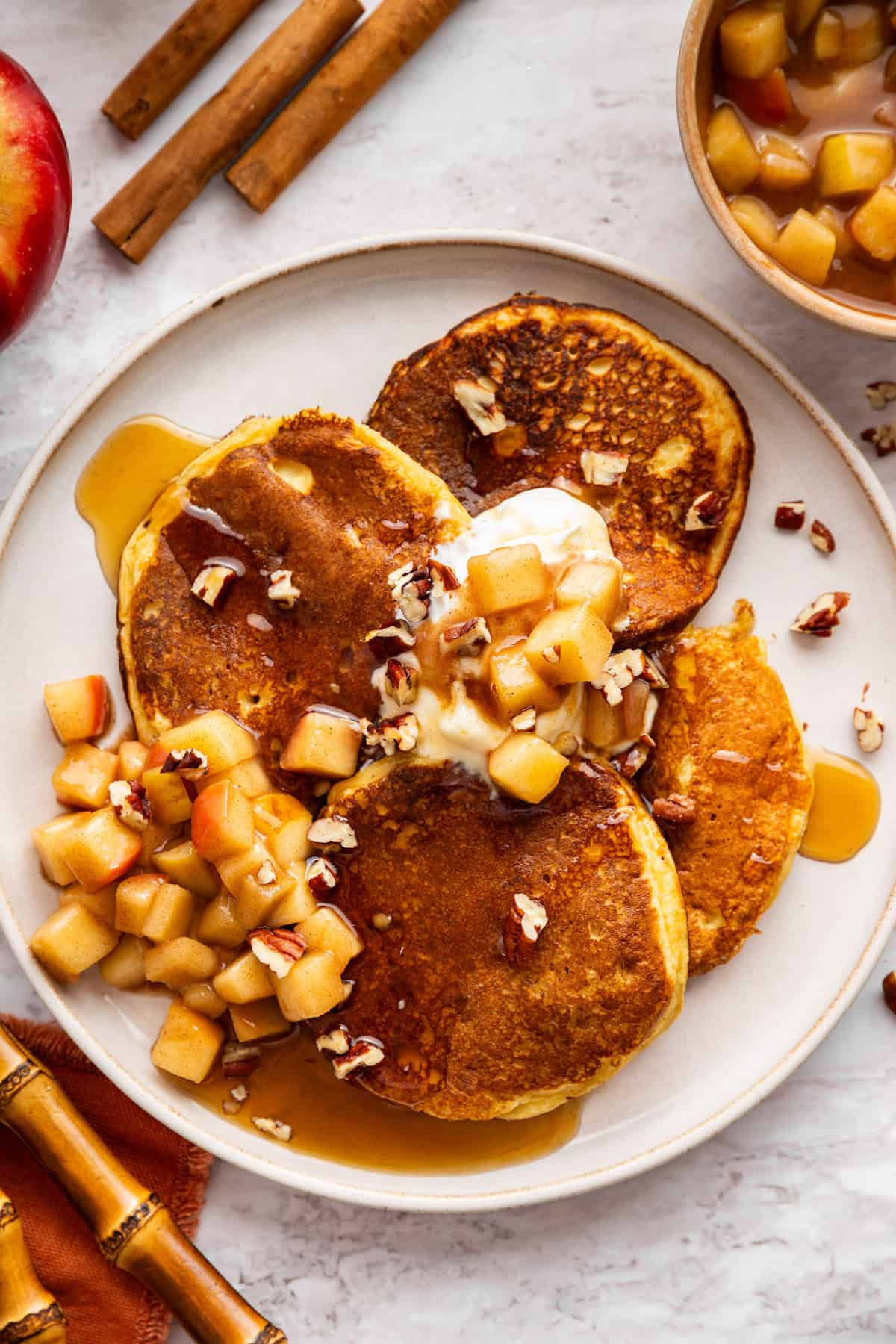 These fluffy apple cider pancakes aren't holding back on apple flavor. The apple cider really does the trick. And that hint of cinnamon? Yes! A plate loaded with apple cider pancakes topped with stewed apples and syrup.