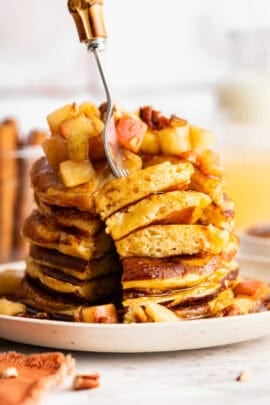 A fork diving into a stack of apple cider pancakes.