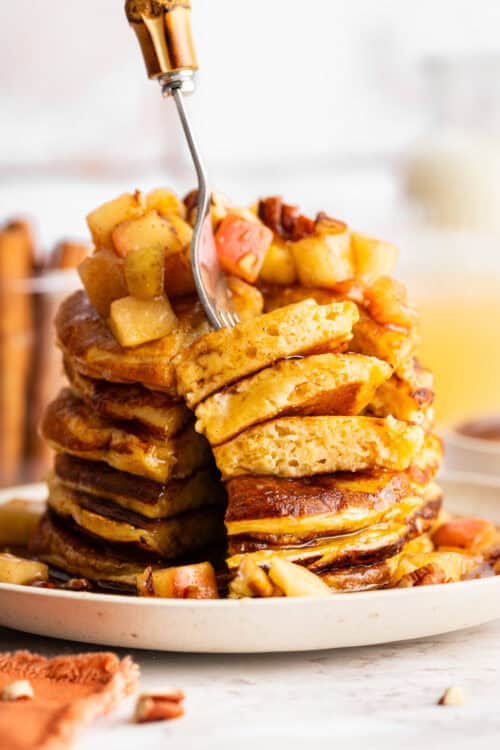 A fork diving into a stack of apple cider pancakes.