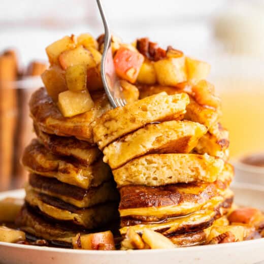 A fork diving into a stack of apple cider pancakes.