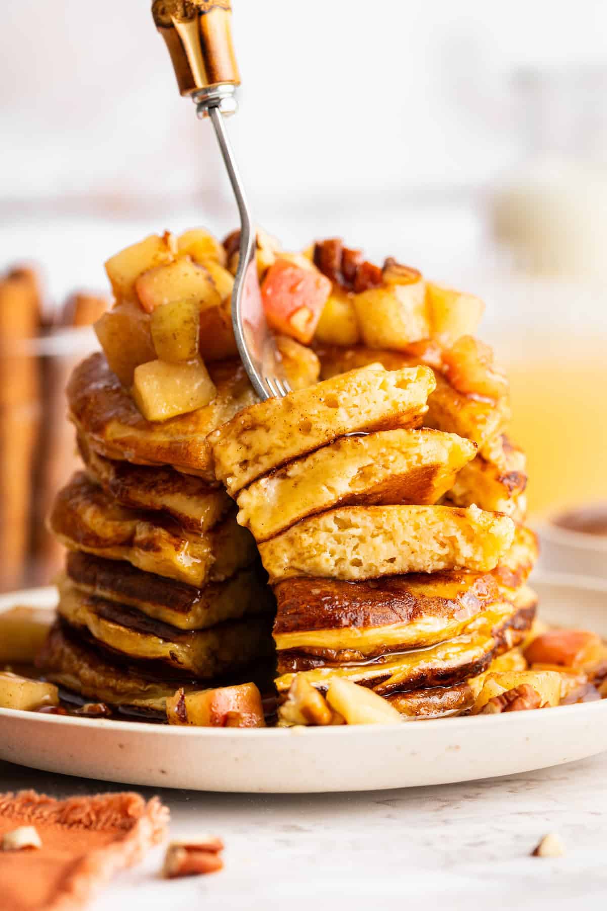 These fluffy apple cider pancakes aren't holding back on apple flavor. The apple cider really does the trick. And that hint of cinnamon? Yes! A fork diving into a stack of apple cider pancakes.