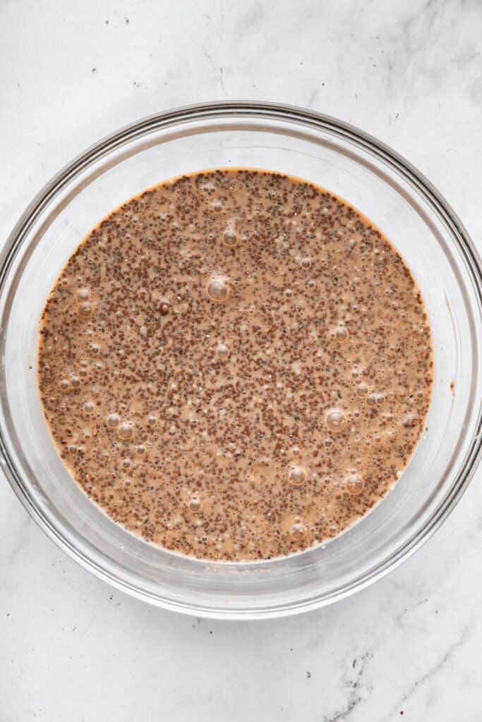 This creamy 5-ingredient chocolate chia pudding packs a powerful punch of protein and just-sweet-enough chocolate pizzaz. And it's so easy! A mixture of chia seeds, hemp seeds, cocoa powder, almond milk, and water in a bowl ready to chill.
