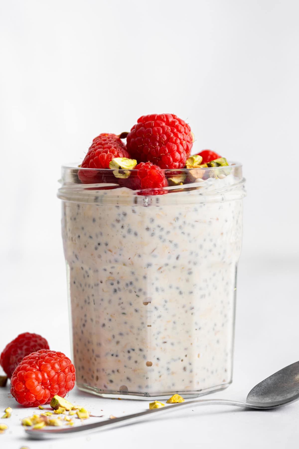 These high-protein overnight oats are so thick and creamy with a little tang from Greek yogurt and a hit of sweetness from maple syrup. Side view of a jar of high protein overnight oats topped with berries and pistachios.