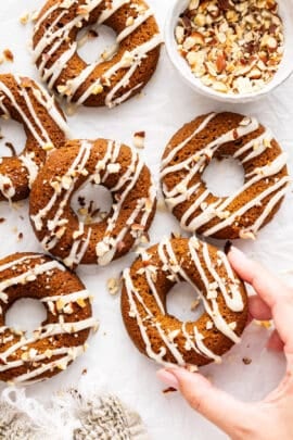 A hand holding a pumpkin donut with coconut-maple glaze.