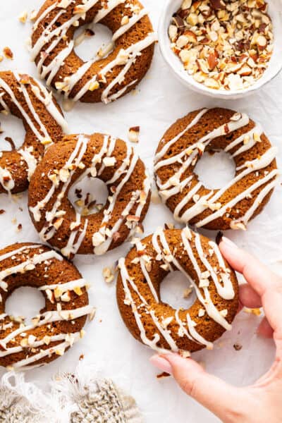 A hand holding a pumpkin donut with coconut-maple glaze.